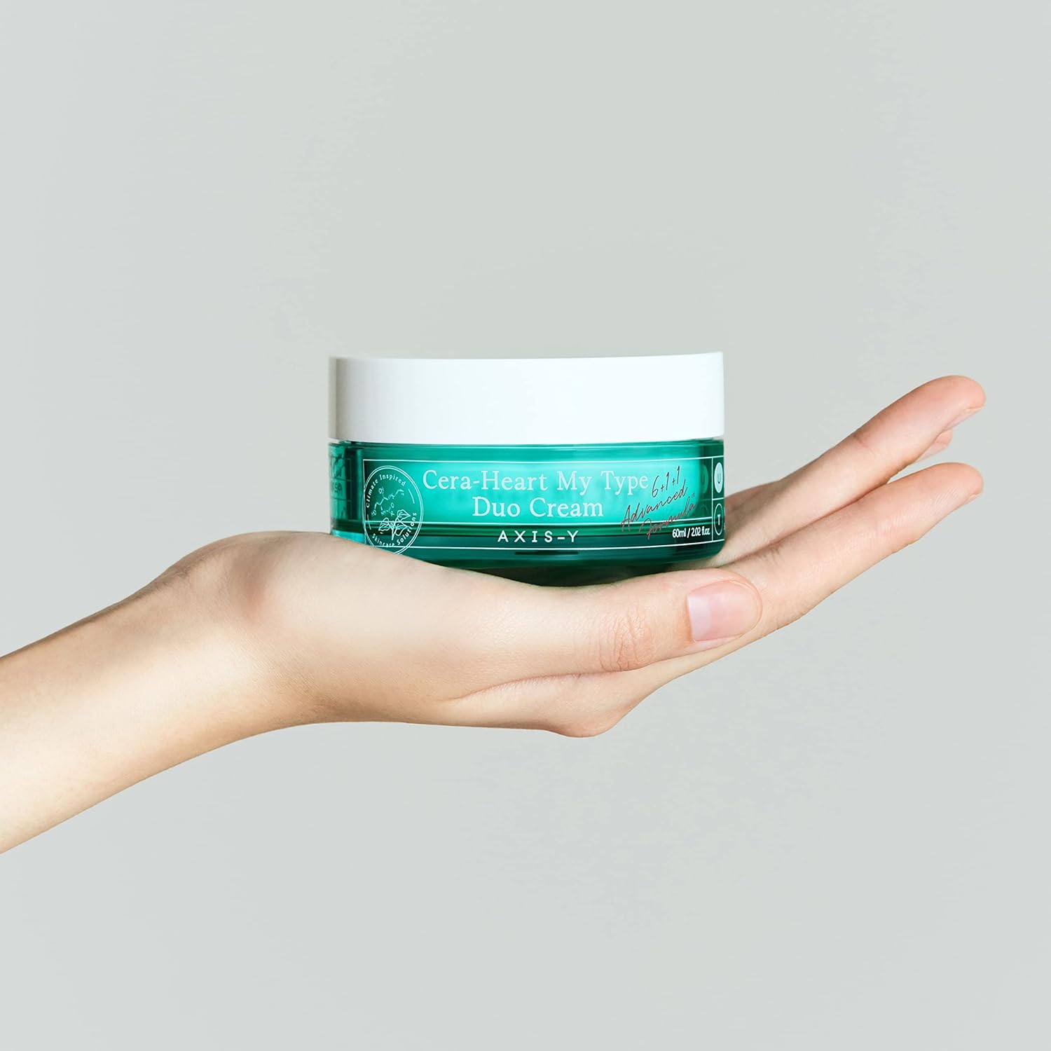 Person holding AXIS-Y Cera-Heart My Type Duo Cream, a Korean moisturizer with dual-function formula for dry and oily skin, in a turquoise jar with white lid.