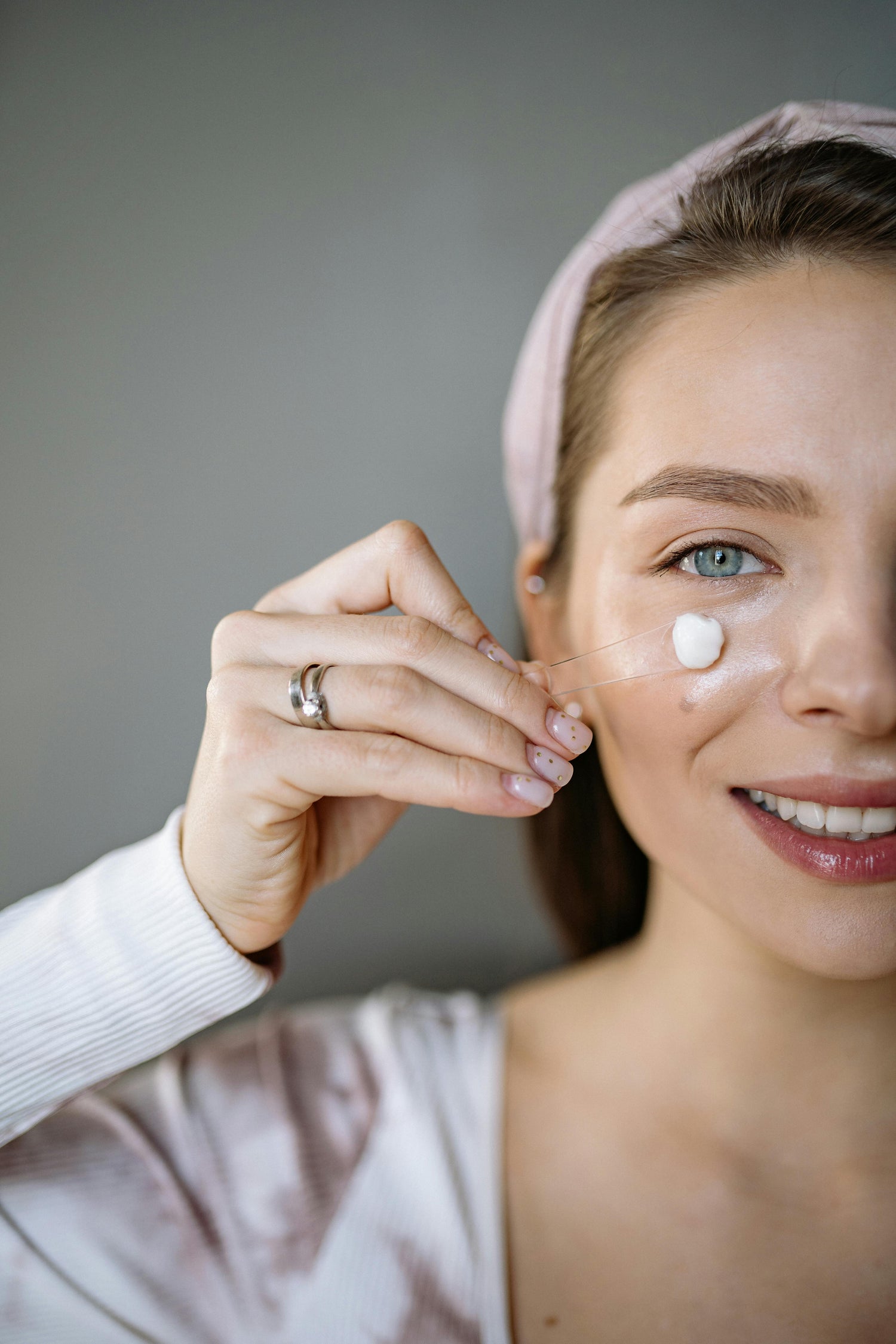 Smiling woman applying eye cream with a spatula during her skincare routine. Glowing skin with The Koko Collection.