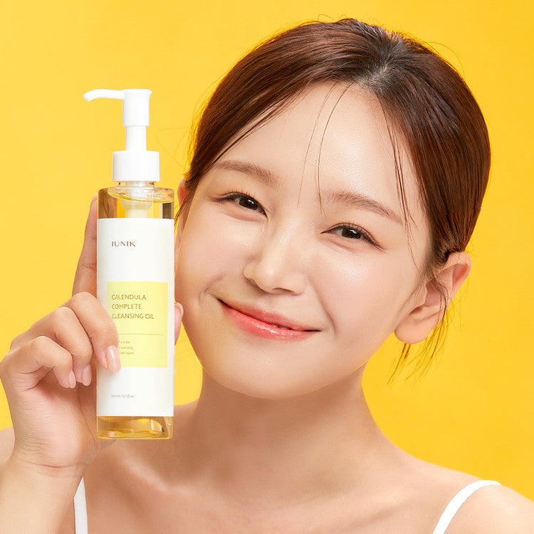 Smiling woman holding iUNIK Calendula Complete Cleansing Oil against yellow background – Korean skincare product for gentle oil cleansing and makeup removal