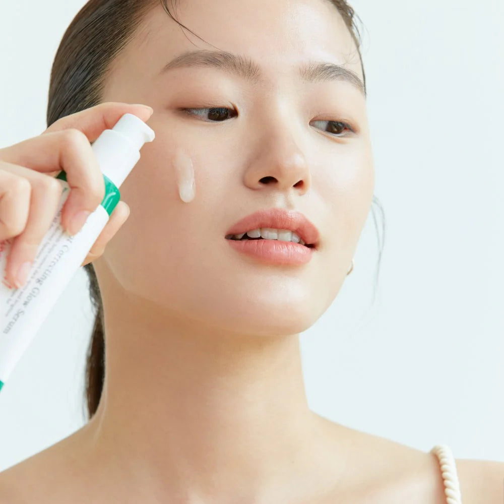 Model applying AXIS-Y Dark Spot Correcting Glow Serum on cheek, featuring brightening skincare for hyperpigmentation and even skin tone.