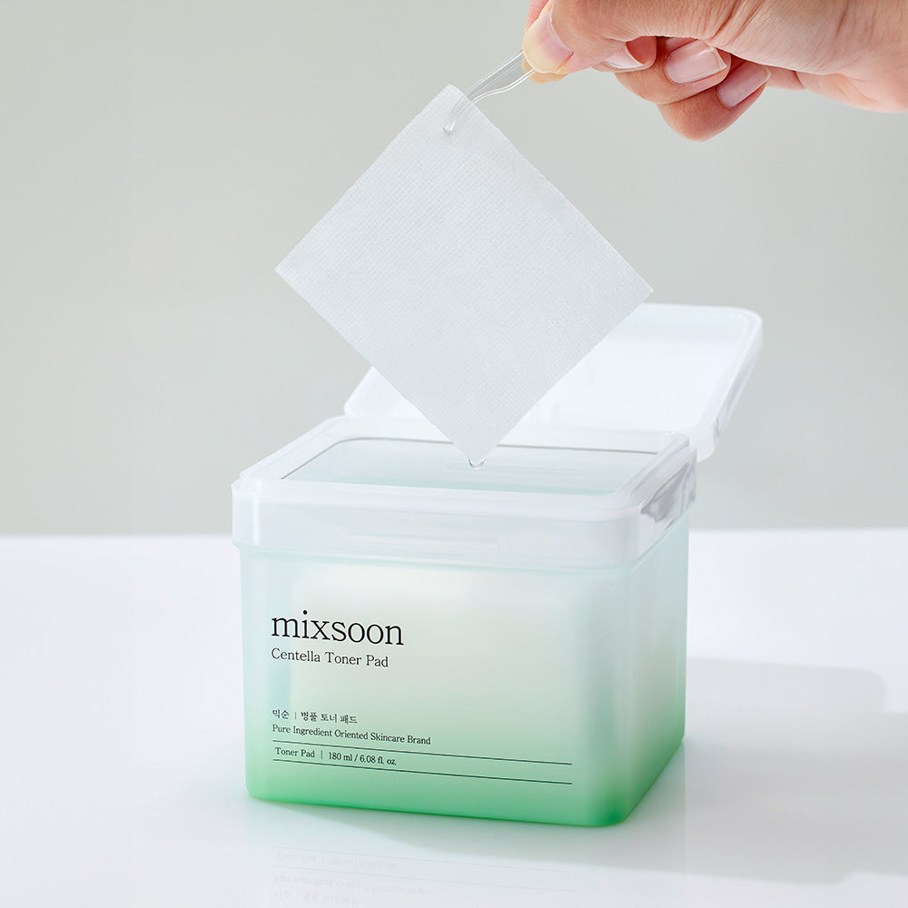 Hand holding a single Mixsoon Centella Toner Pad with tweezers above open container, showcasing calming skincare for sensitive and irritated skin.