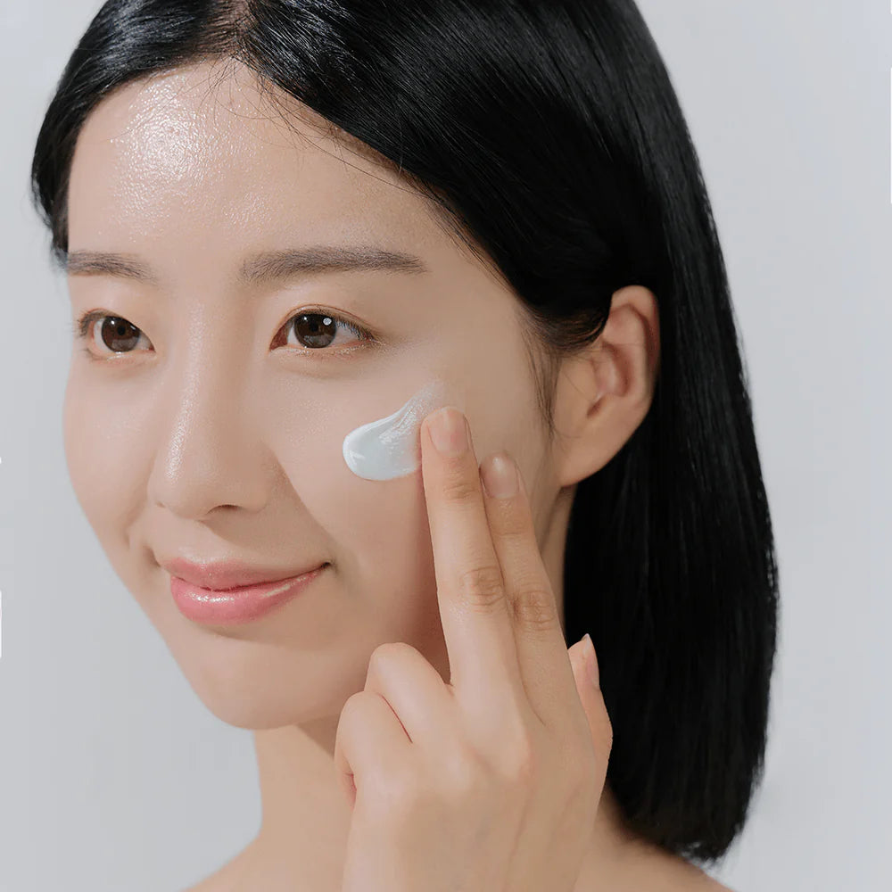 Woman applying SKIN1004 Hyalu-Cica sunscreen to cheek with soft natural finish